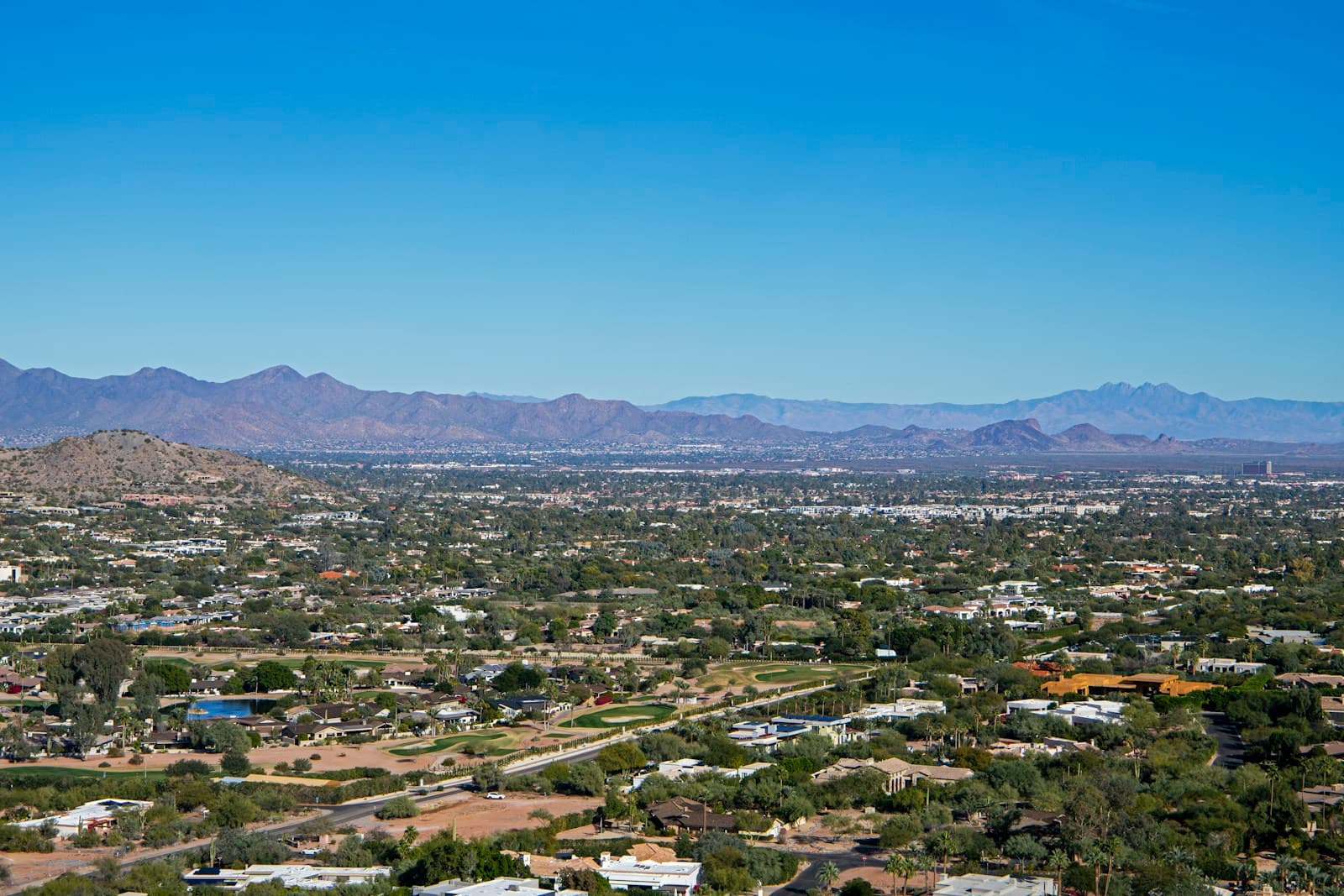 Aerial view of desert suburban landscape with mountains in background under clear blue sky